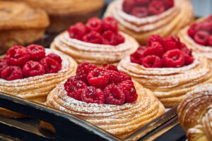 Fresh raspberry danish pastries topped with powdered sugar displayed on a bakery tray.