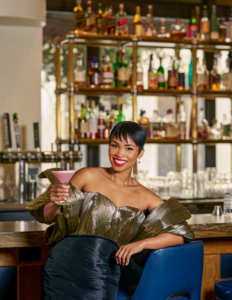 Woman leans at a bar holding up a cocktail to display a Bloom cocktail as a part of the Local Garden program